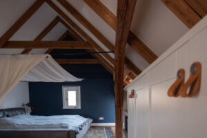 Casa Malina Interior Design Hamburg – Schlafzimmer im Dachgeschoss mit Holzbalken und dunkelblauer Akzentwand
